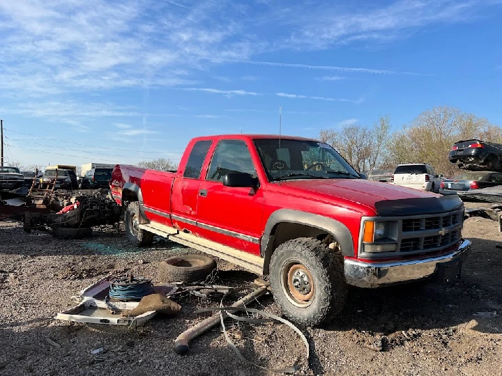 Red pickup truck in a junkyard with debris.