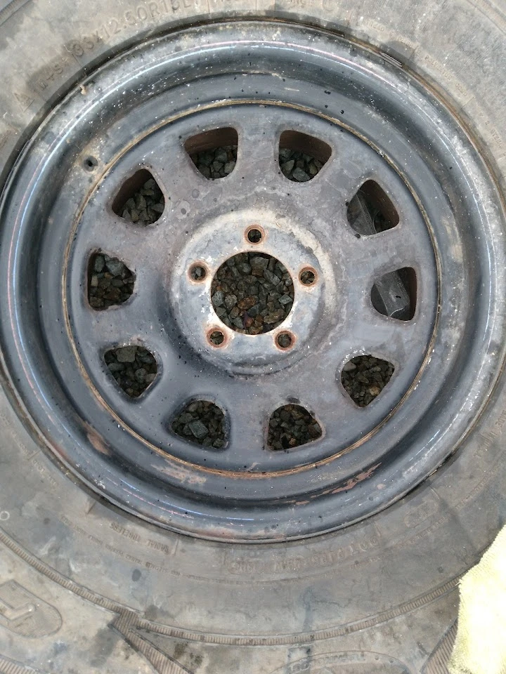 Rusty wheel rim with a worn tire and gravel.