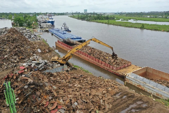 Scrap metal being loaded onto a barge by a crane.