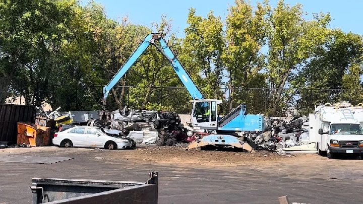 Scrapyard with heavy machinery and stacked vehicles.