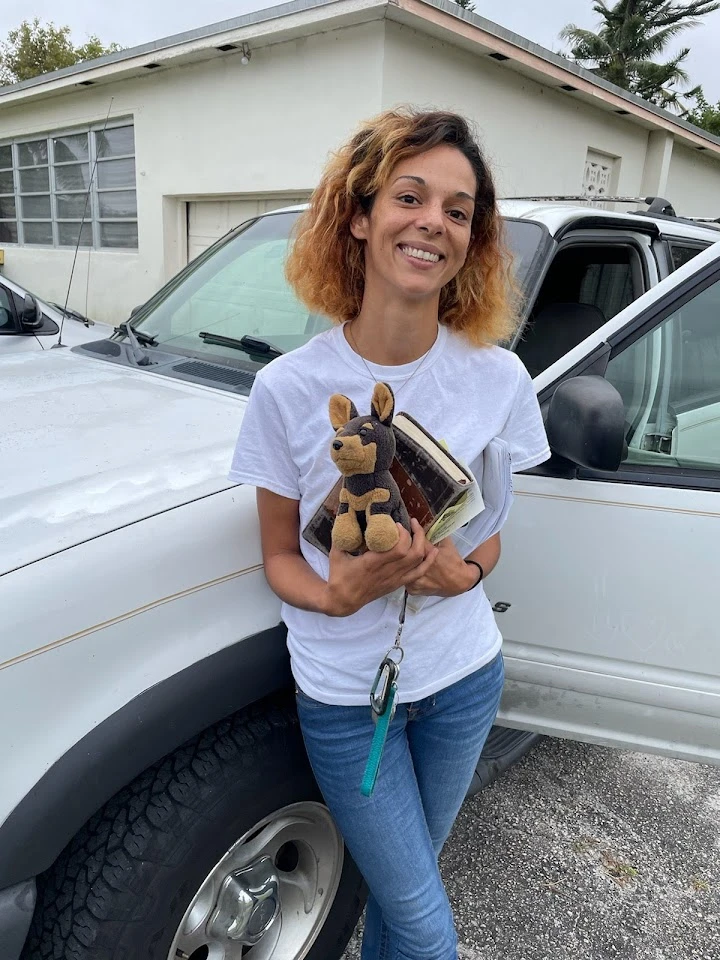 Smiling woman with a toy dog by a pickup truck.