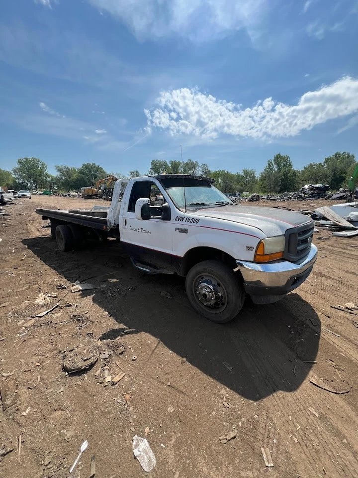 Tow truck in a junkyard under a blue sky.