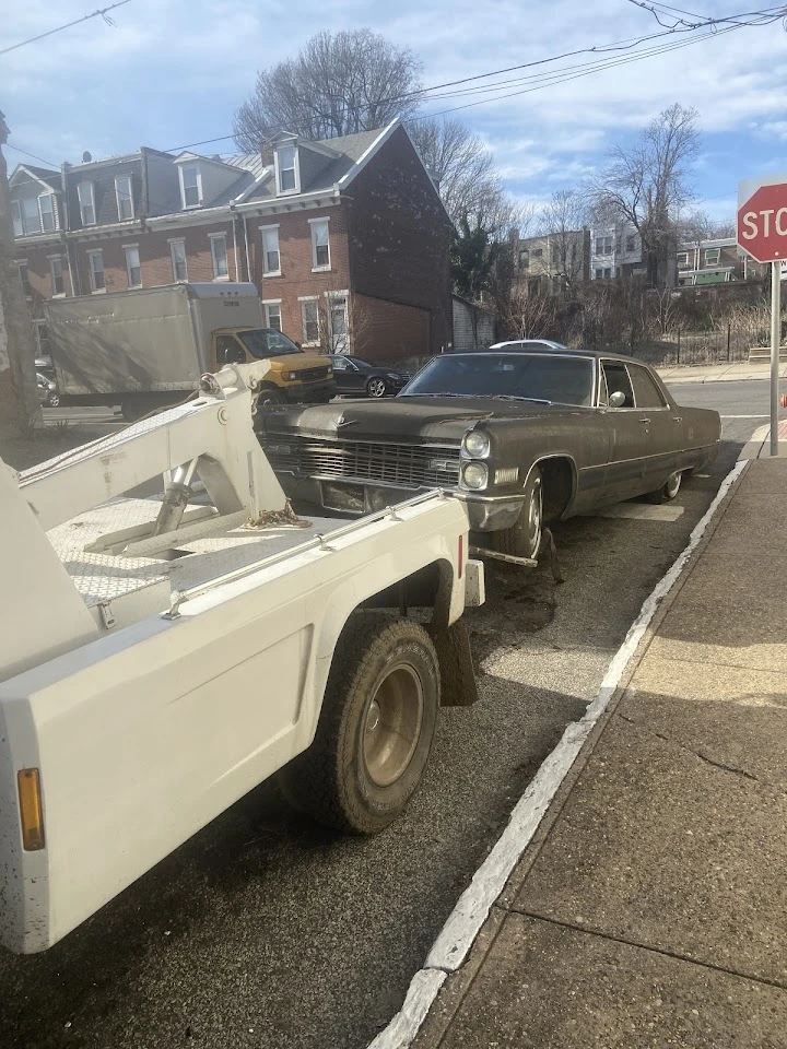 Tow truck lifting a classic junk car on the street.