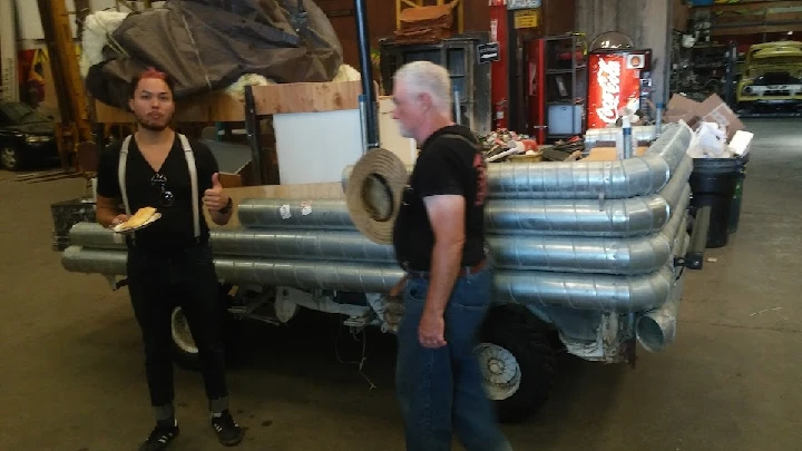 Two men beside a unique vehicle with metal pipes.