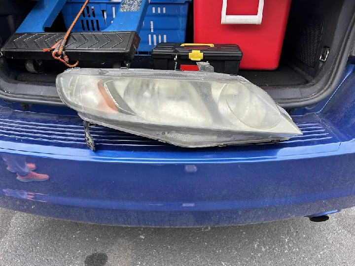 Used car headlight resting on a blue vehicle's trunk.