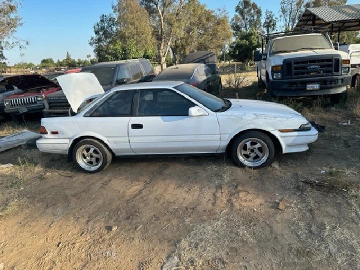 White car parked in a salvage yard.