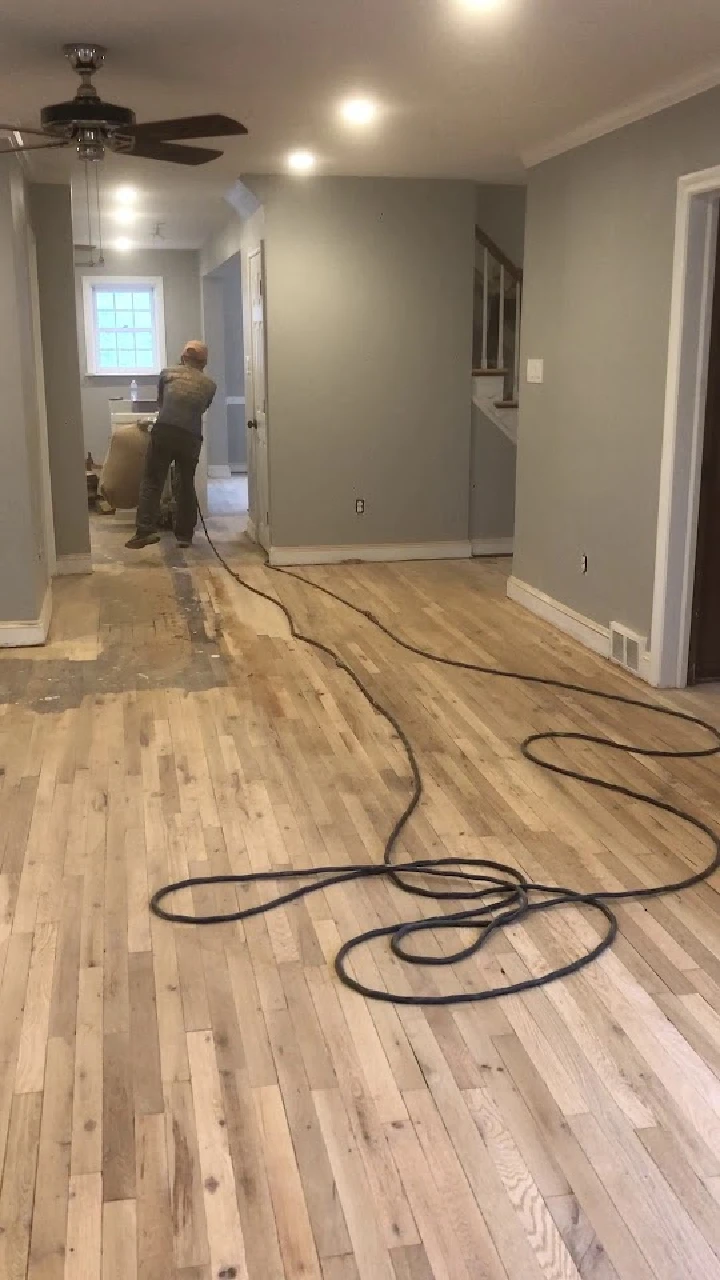 Worker refinishing wooden floor in a hallway.