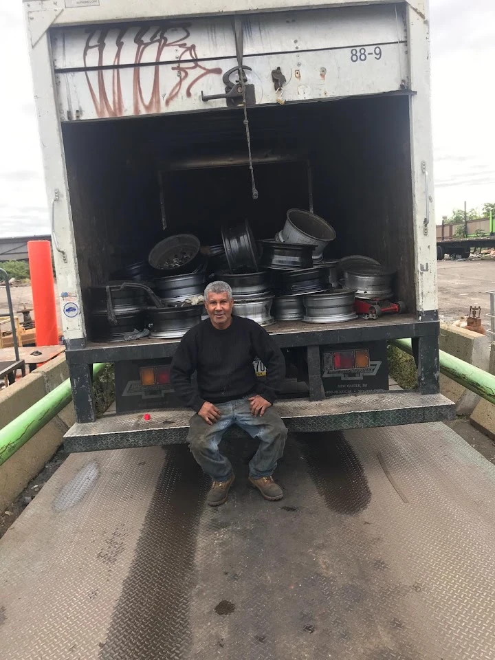 Worker sitting on truck with rims in background.