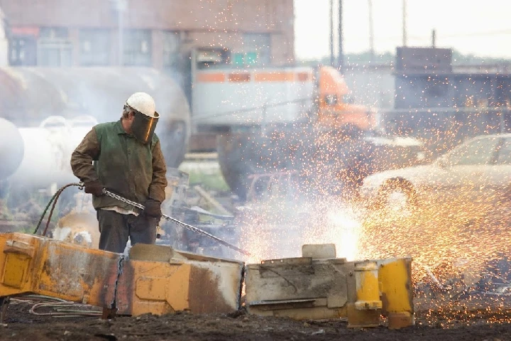 Worker using a torch, sparks flying in recycling yard.