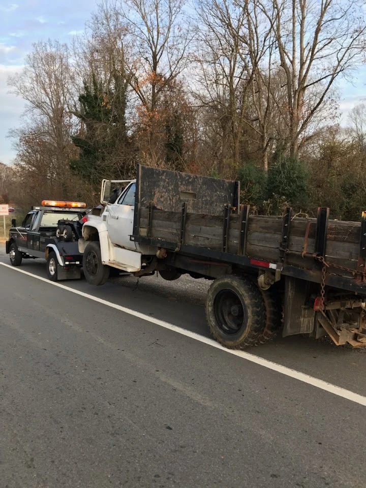 Wrecker service towing a damaged truck roadside.