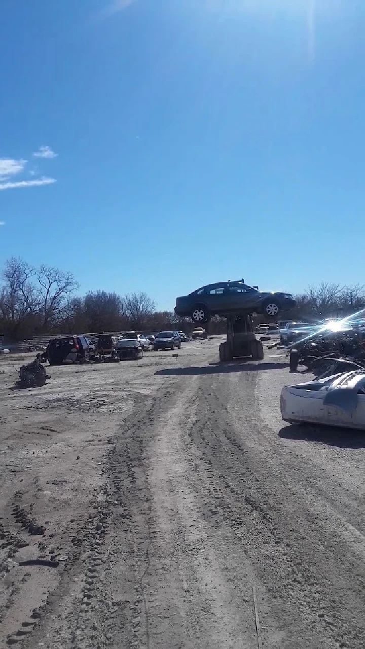 Auto recycling yard with stacked vehicles and blue sky.