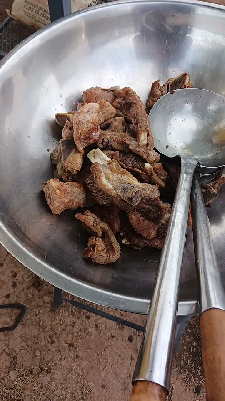 Bowl of cooked meat with metal serving utensils.