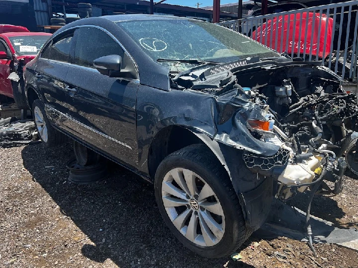 Damaged black car at auto salvage yard.