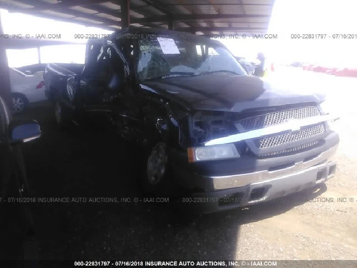 Damaged black pickup truck in salvage yard.