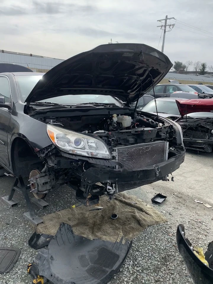 Damaged car with open hood in junkyard setting.