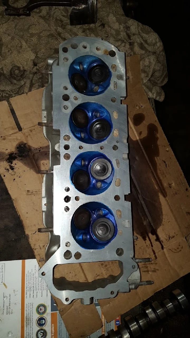 Engine head with blue valves on a workbench.