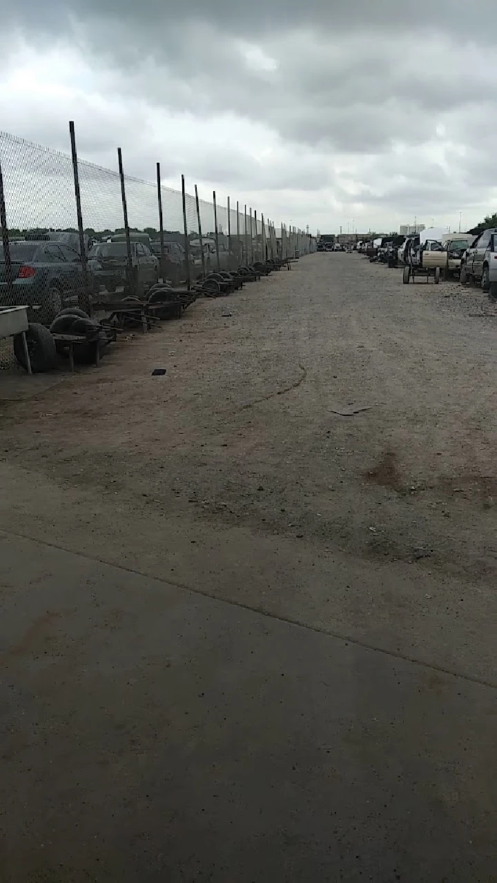 Gravel path lined with vehicles and fences.