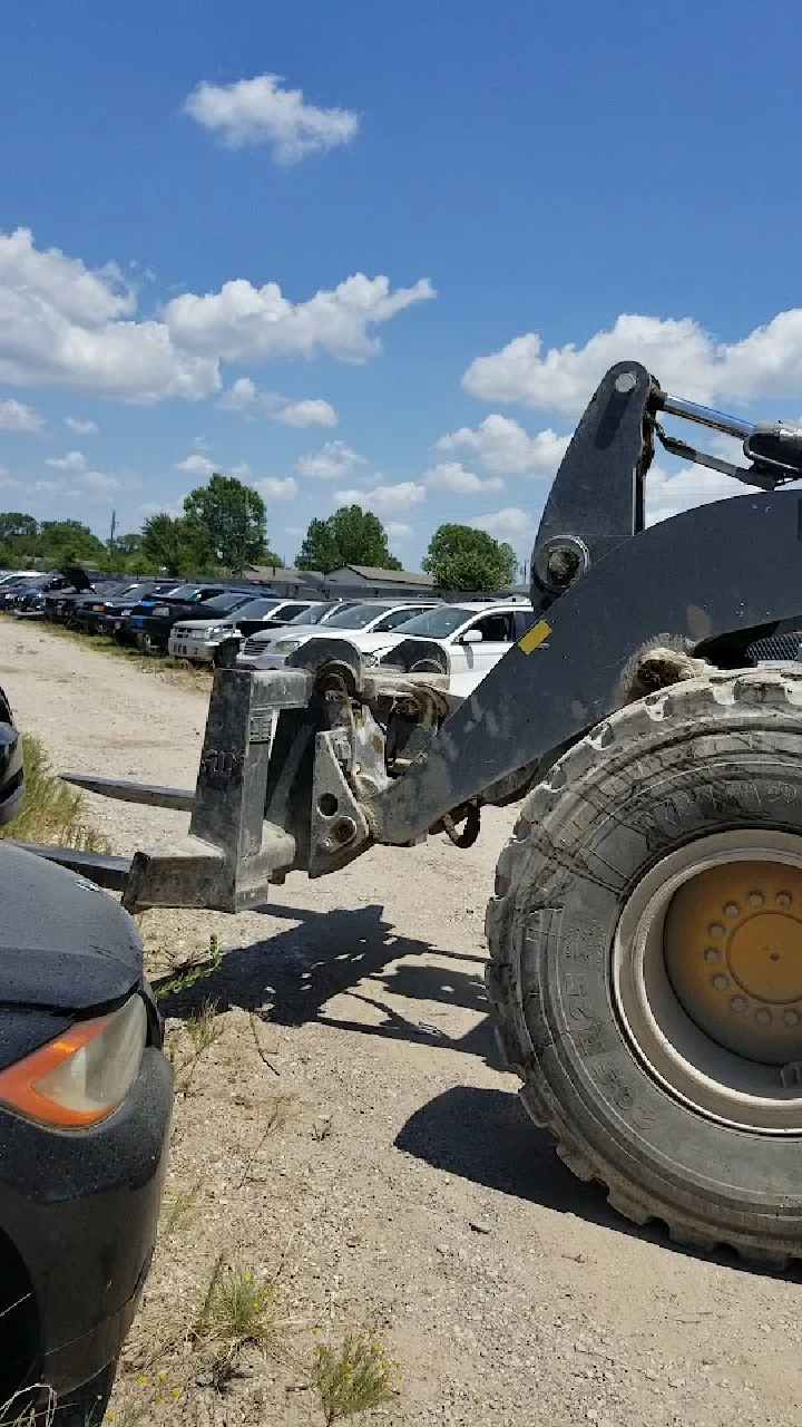 Heavy machinery in a salvage yard with parked cars.