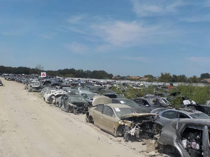 Junkyard filled with abandoned vehicles under blue sky.