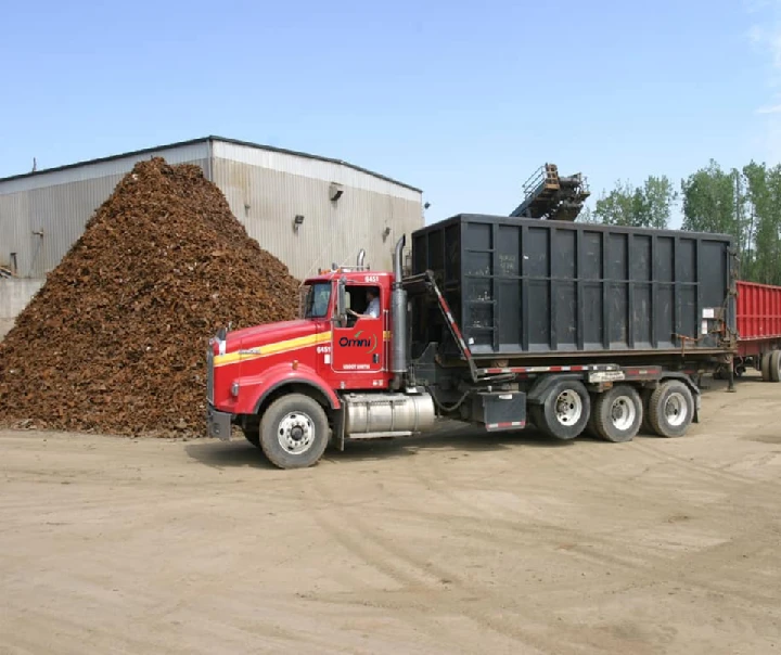 Red dumpster truck next to a large scrap pile.