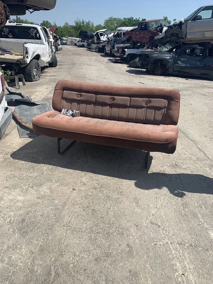 Sofa in a metal salvage yard among discarded vehicles.