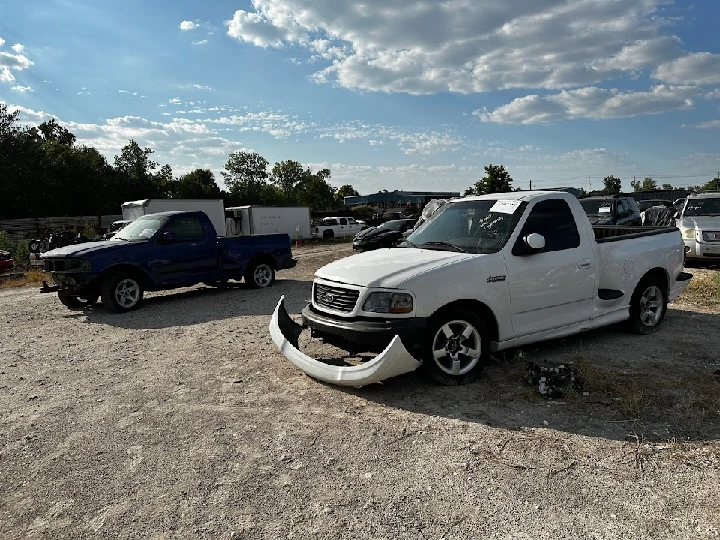 Two salvage trucks in a sunlit auto yard.