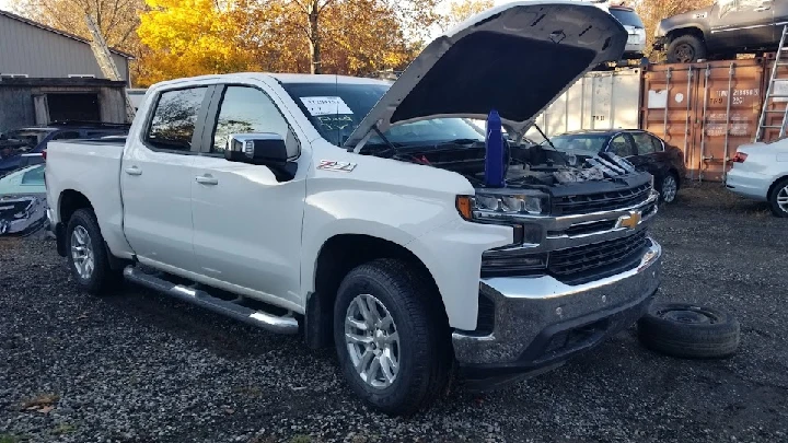 White pickup truck with the hood open in a salvage yard.