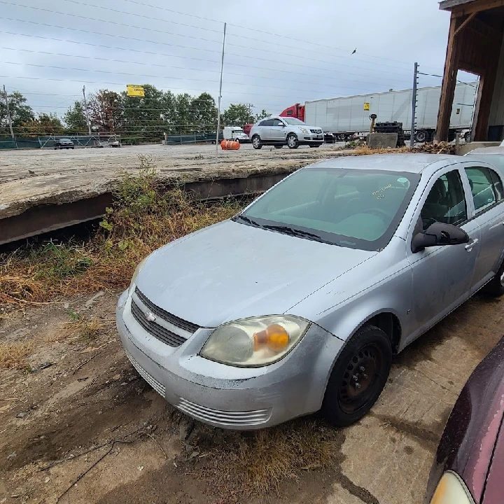 Abandoned silver sedan in a junkyard.