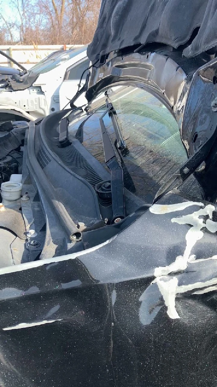 Car hood and windshield close-up in an auto parts yard.