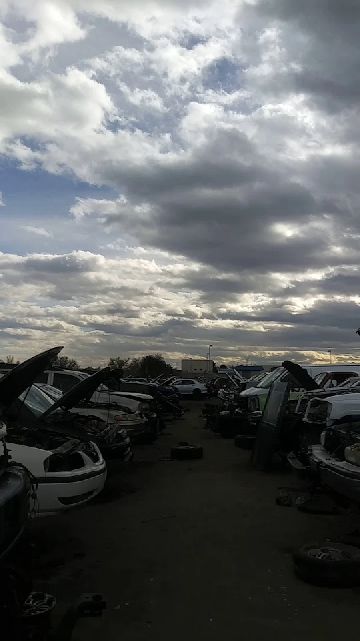 Car junkyard with cloudy sky above.