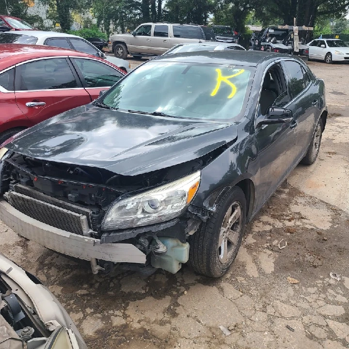 Damaged black car in a junkyard lot.