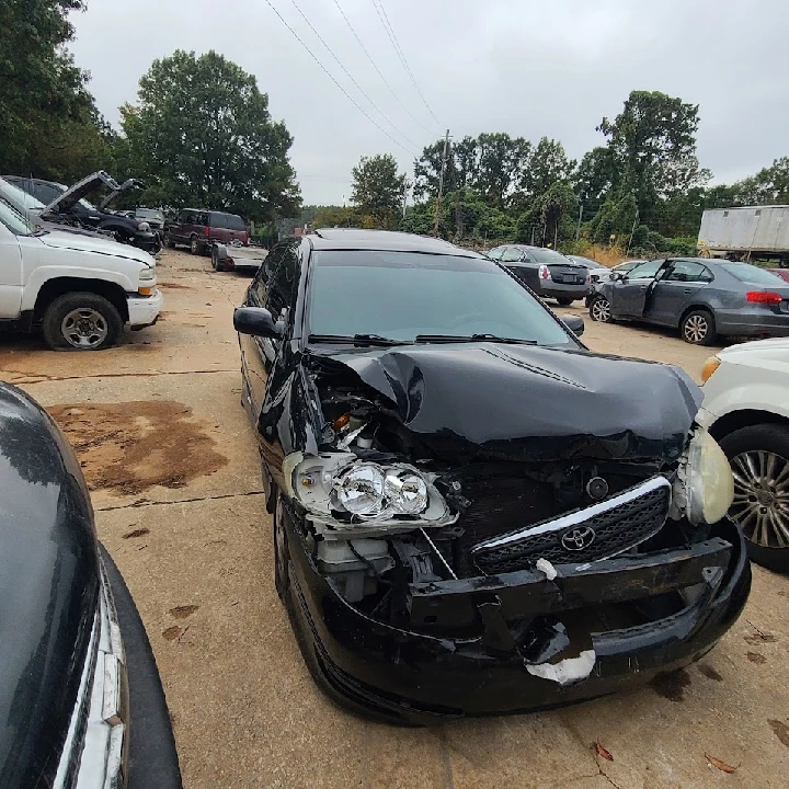 Damaged black car in a junkyard setting.