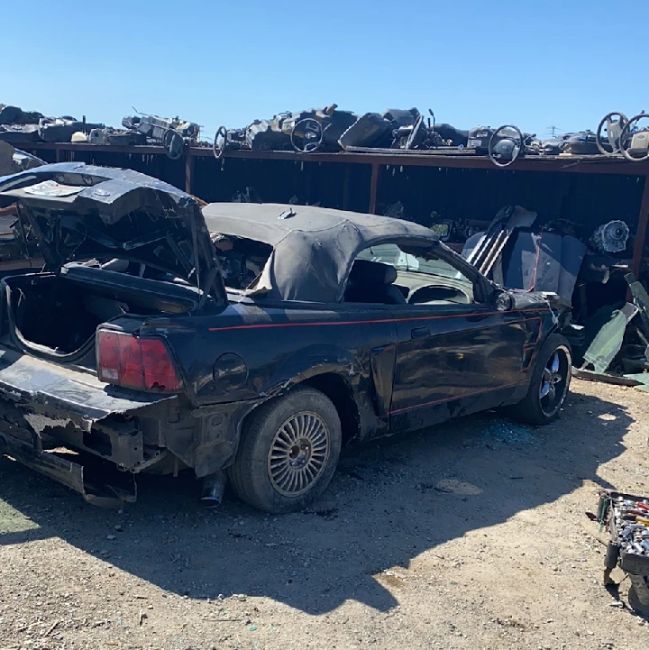 Damaged black convertible in a junkyard.