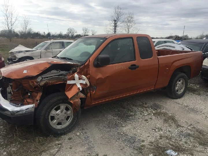 Damaged orange pickup truck at auto salvage yard.