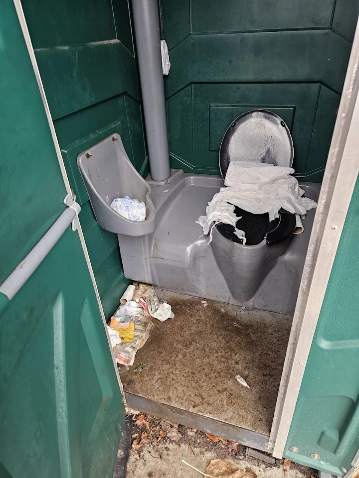 Dirty portable toilet interior with trash and waste.