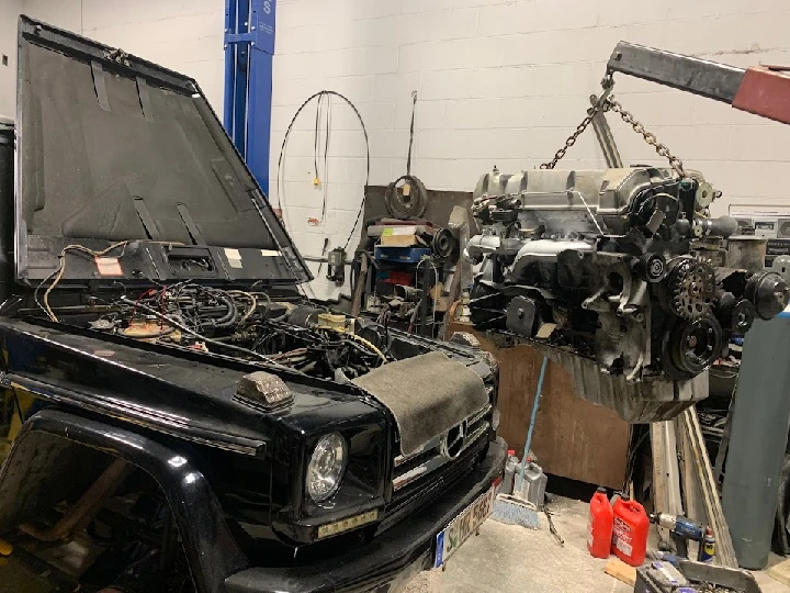 Engine being removed from a black vehicle in a shop.