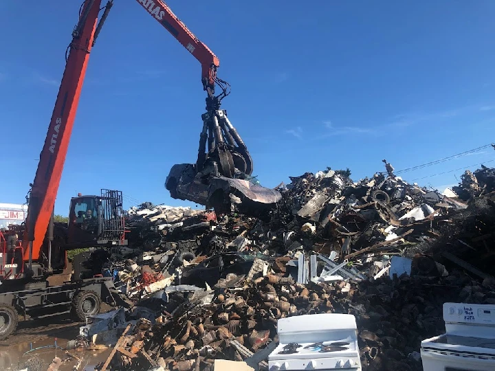 Excavator lifting scrap metal at recycling facility.