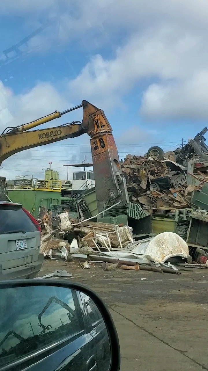 Excavator lifting scrap metal at recycling yard.