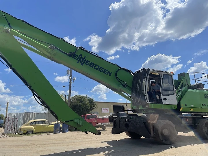 Green recycling machine in operation against blue sky.