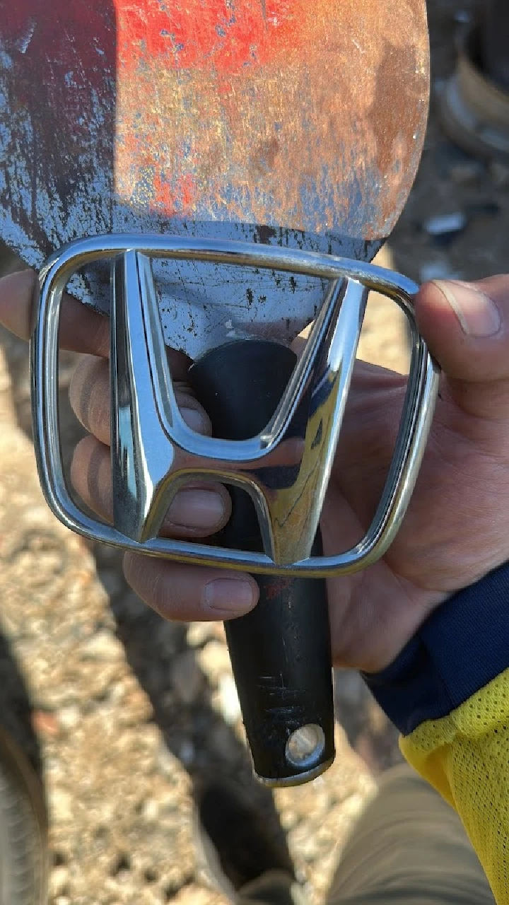 Hand holding a chrome Honda emblem and tool.