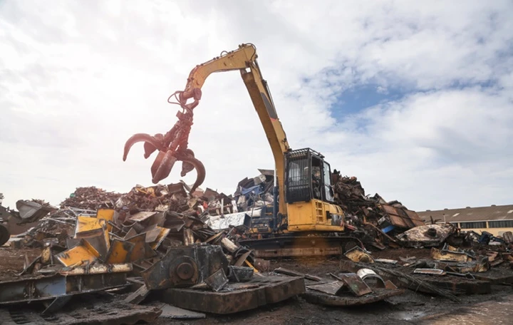 Heavy machinery lifting scrap metal at a junkyard.