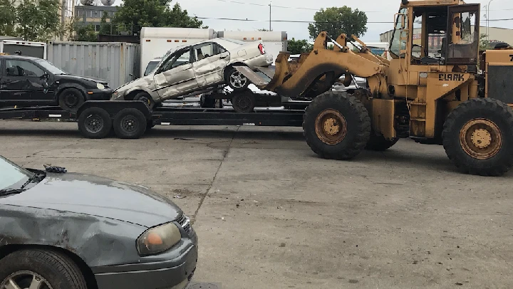 Heavy machinery loading cars onto a flatbed trailer.