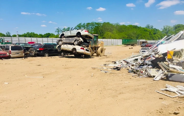 Heavy machinery stacking old cars at a recycling yard.