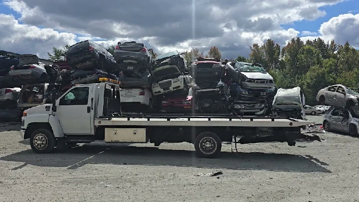 Junk cars stacked on a tow truck at a yard.