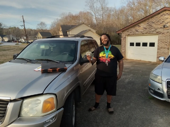 Man holding cash next to a junk car outdoors.