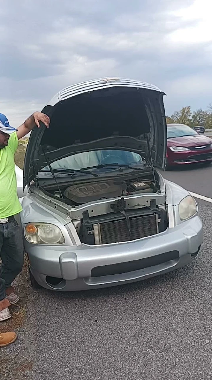 Man inspecting the engine of a silver car.