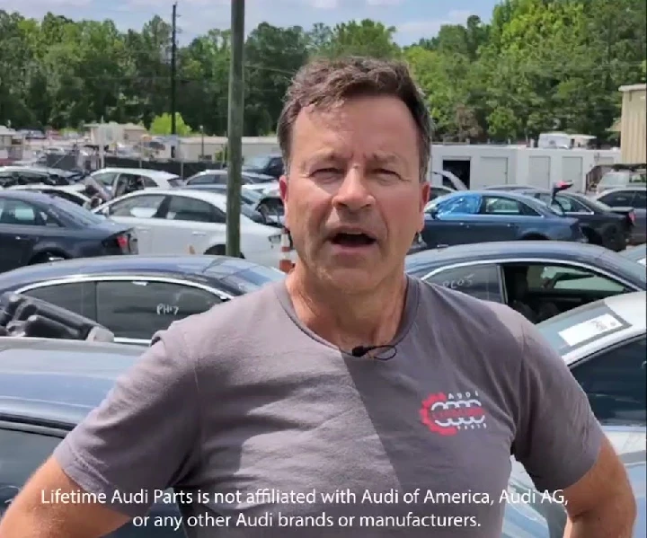 Man speaking in a junkyard surrounded by cars.