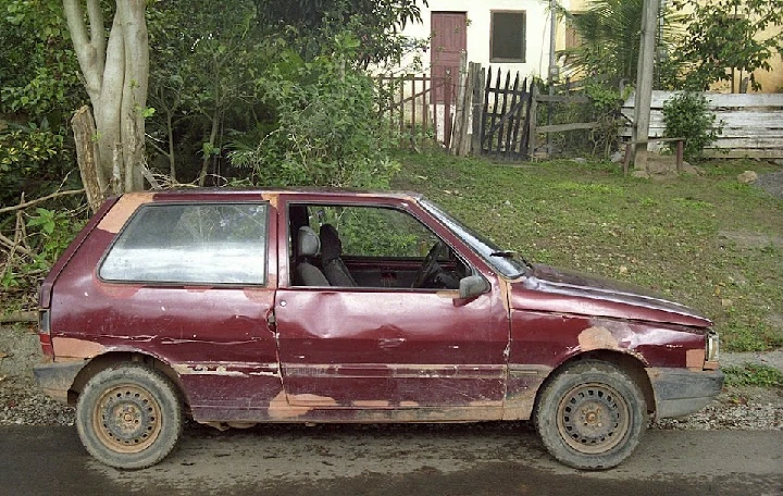 Old, damaged car parked in a grassy area.