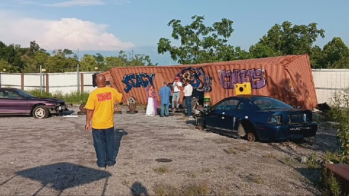 People interacting near cars and a shipping container.