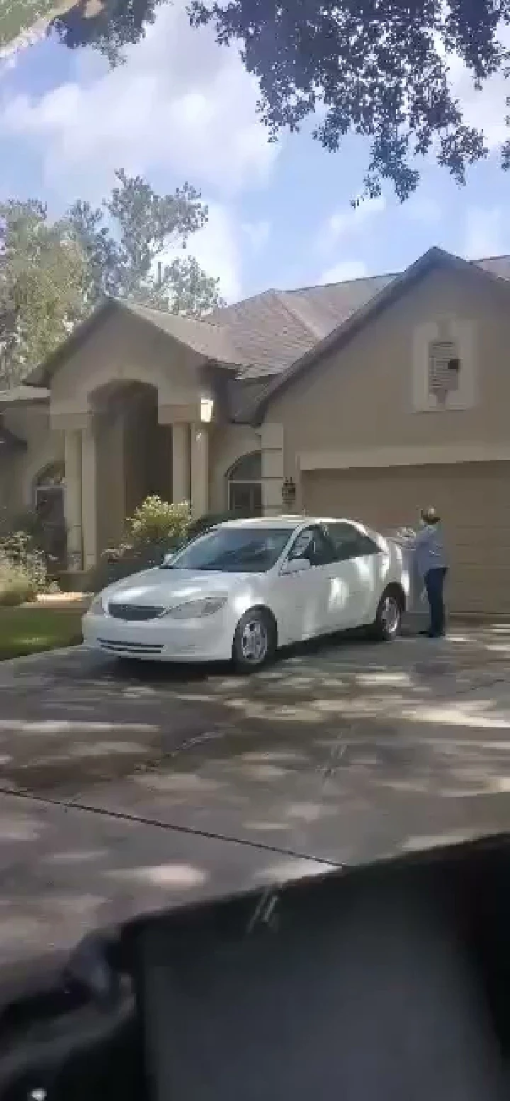 Person checking a white car in front of a house.